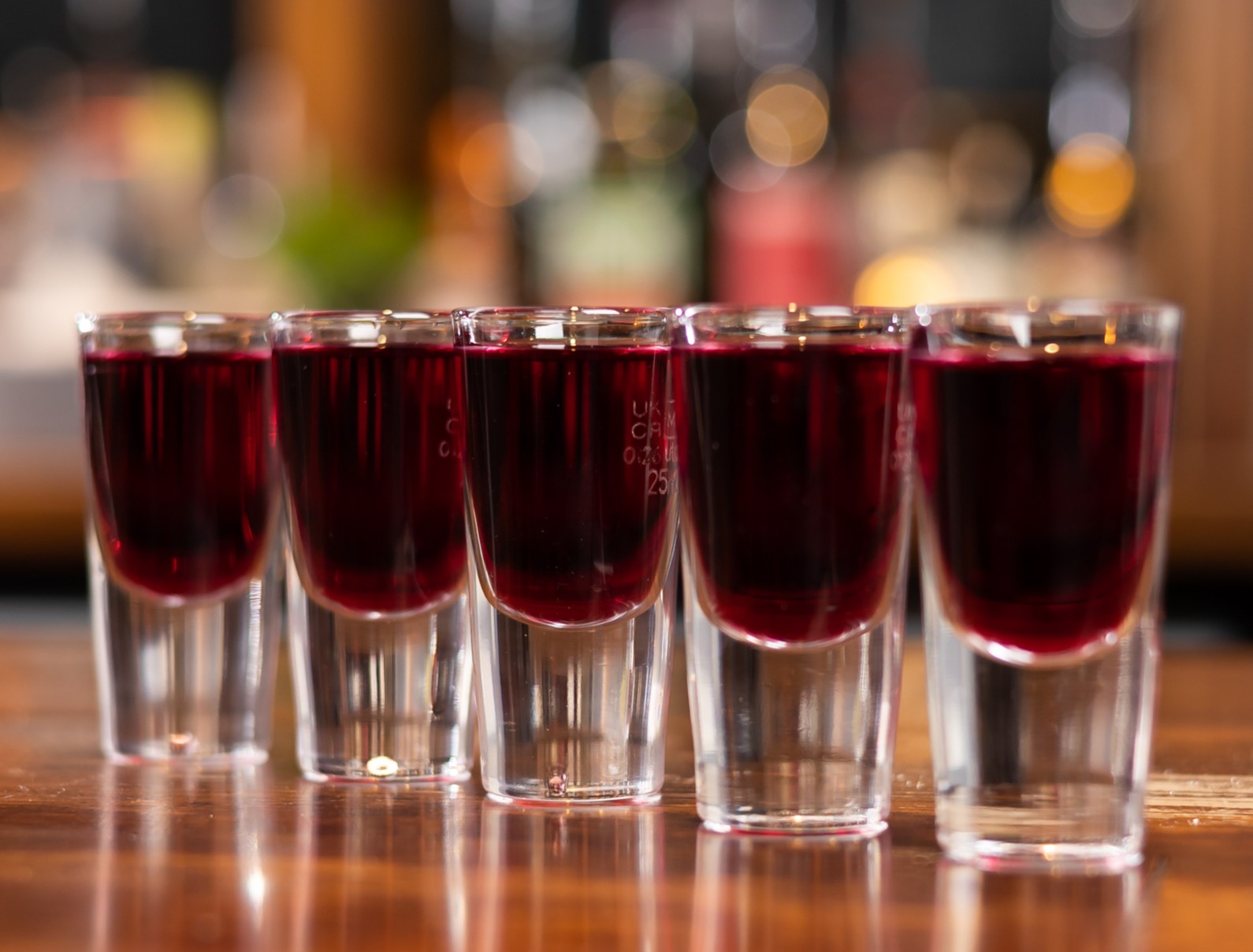 Several shots aligned neatly on a bar. The shots are dark brown in colour. The background is blurred.