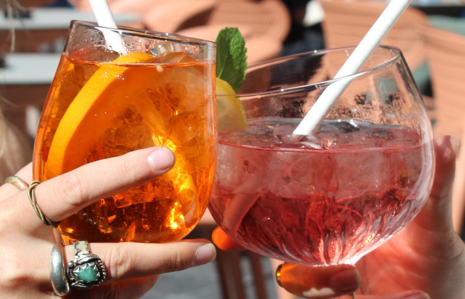 Two large glasses one with an orange spritz and the other a refreshing looking cocktail with a lemon and mint garnish.
